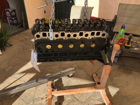 1992 Jeep Wrangler - A black V8 engine block is mounted on an orange engine stand, suspended by chains from an overhead hoist. Various tools and a bottle of cle…