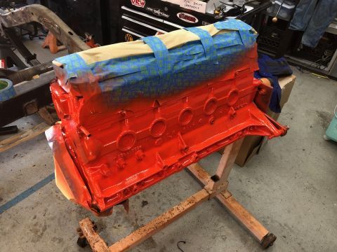 1992 Jeep Wrangler - A bright orange painted engine block is masked with blue painter's tape and tan paper, resting on a wooden stand in a garage. The engine bl…