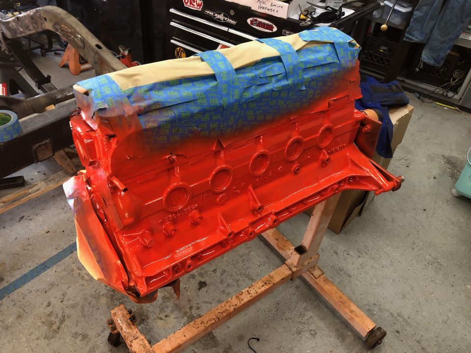 Orange painted engine block on a stand, masked for painting.
