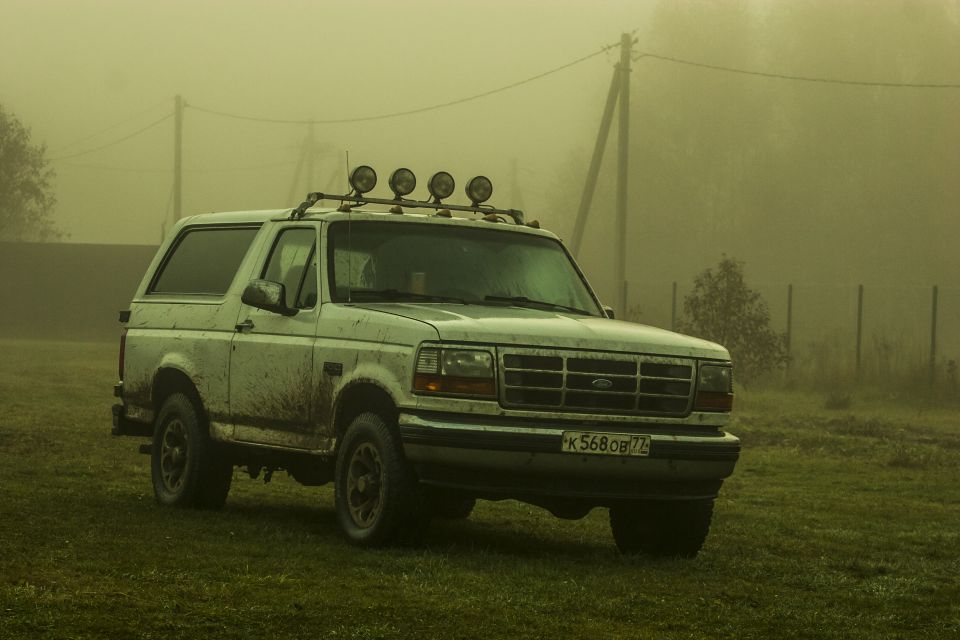 1993 Ford Bronco in a foggy field with a roof rack and auxiliary lights.