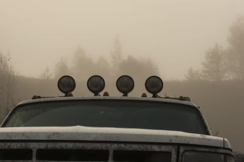 1993 Ford Bronco - The front of a white, dusty truck is visible in a foggy environment, featuring a row of four round spotlights mounted on the roof.