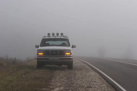 1993 Ford Bronco - A white Ford Bronco is parked on the side of a road on a foggy day. The vehicle has four auxiliary lights mounted on the roof rack.