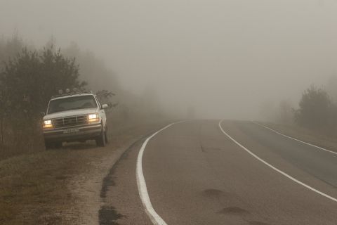 1993 Ford Bronco - A white Ford Bronco is parked on the side of a road on a foggy day. The vehicle is facing the camera with its headlights on.