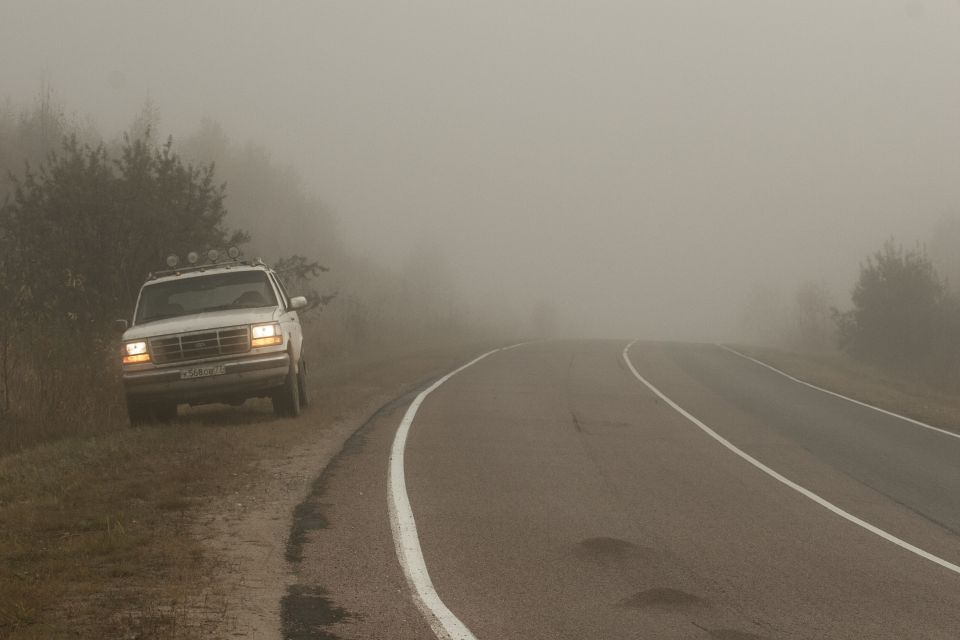 White Ford Bronco parked on the side of a foggy road, headlights on.