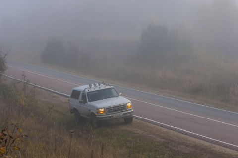 1993 Ford Bronco - A white Ford Bronco is parked on the shoulder of a road on a foggy morning. The SUV has a roof rack with four auxiliary lights.