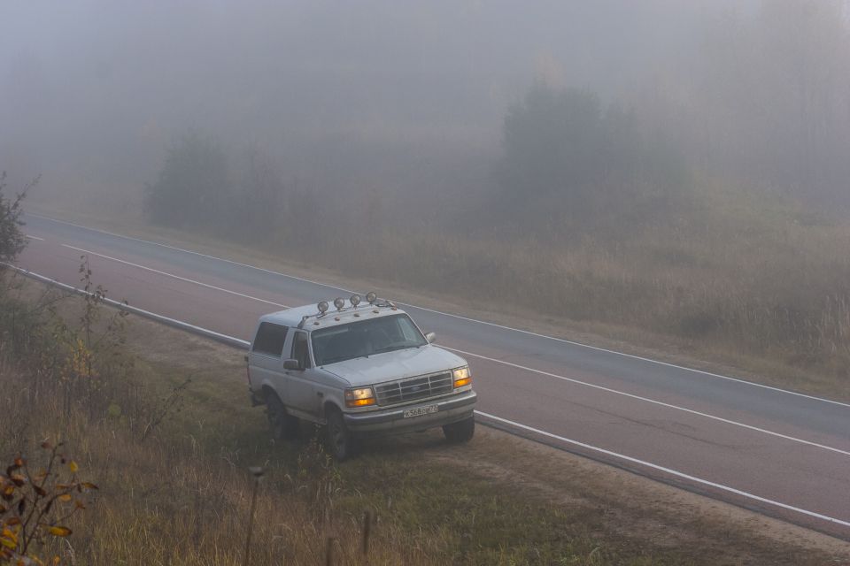 White Ford Bronco with roof rack lights on a foggy road.