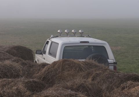 1993 Ford Bronco - A white Ford Bronco is parked in a field, partially obscured by large round hay bales. The vehicle has a light bar with four spotlights mou…