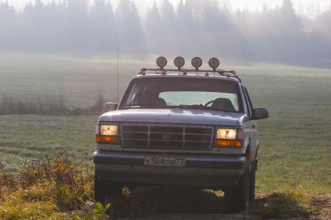 1993 Ford Bronco - A silver 1993 Ford Bronco is parked on a dirt path in a foggy field with trees in the background. The vehicle has four auxiliary lights mou…
