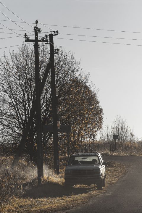 1993 Ford Bronco - A dark-colored SUV is parked on the side of a dirt road next to a utility pole and trees. The vehicle has four auxiliary lights mounted on…