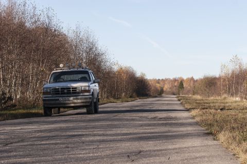 1993 Ford Bronco - A silver 1993 Ford Bronco is parked on the side of a paved road with trees lining the left side of the road and a field on the right. The v…