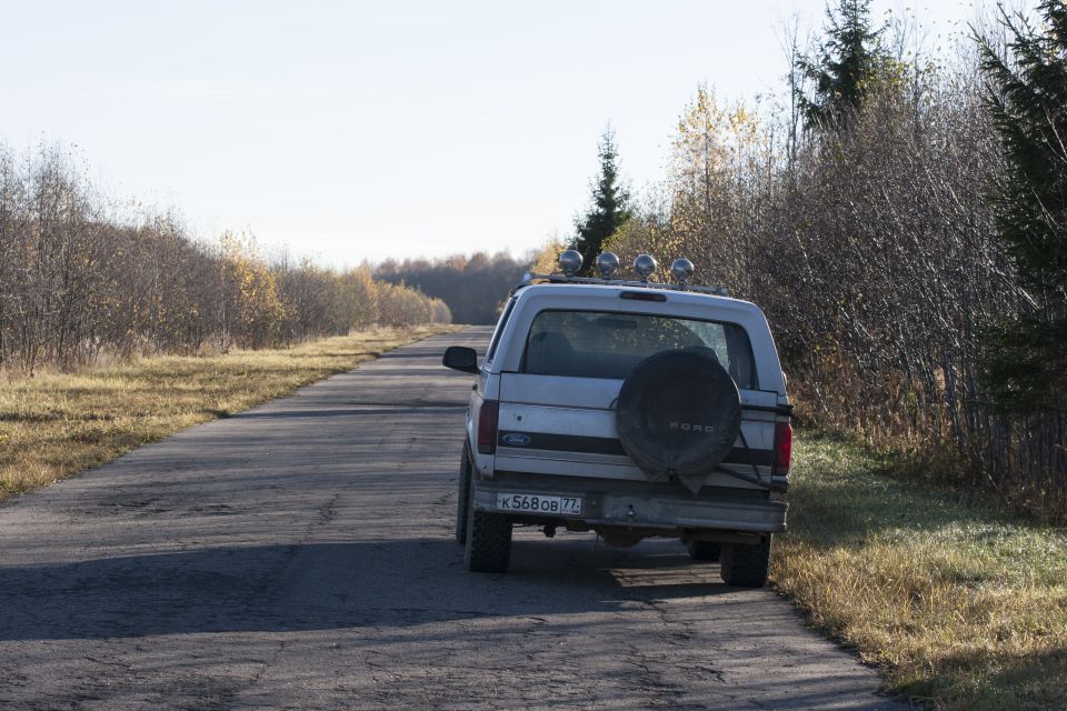 Silver Ford Bronco parked on a rural road, rear view, with spare tire and roof lights.