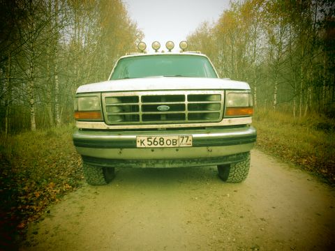 1993 Ford Bronco - The front view of a white Ford Bronco is parked on a dirt road surrounded by trees in autumn. The vehicle has a license plate that reads "K…