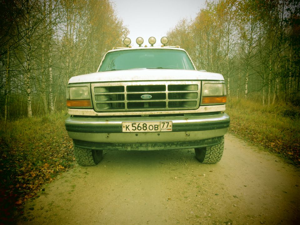 1993 Ford Bronco front view on a dirt road with autumn trees.