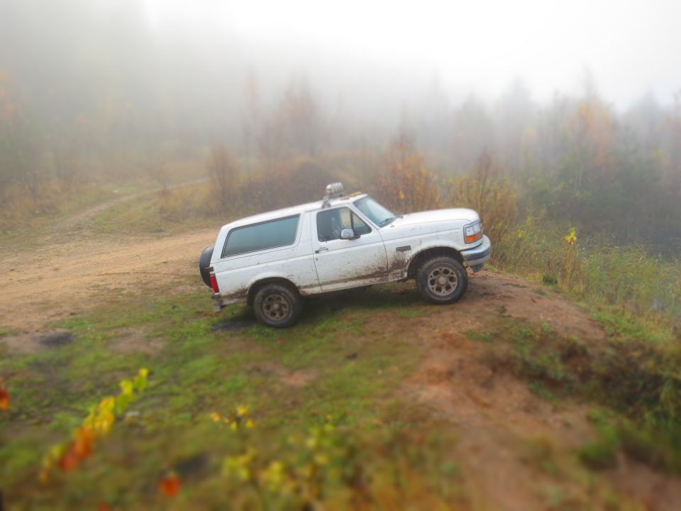 White Ford Bronco parked on a dirt hill in foggy, wooded terrain.