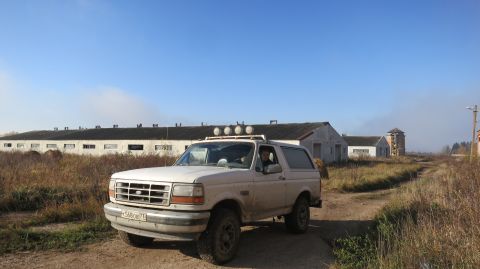 1993 Ford Bronco - A white Ford Bronco is parked on a dirt road in front of a row of long, low buildings and a silo. The vehicle has four auxiliary lights mou…