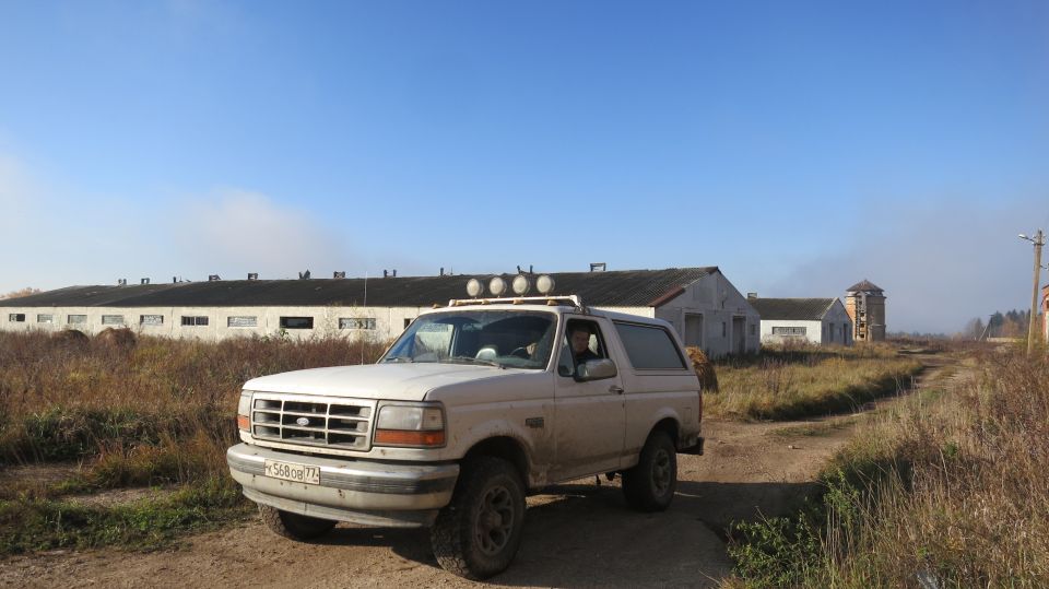 White Ford Bronco parked on dirt road with buildings in the background.