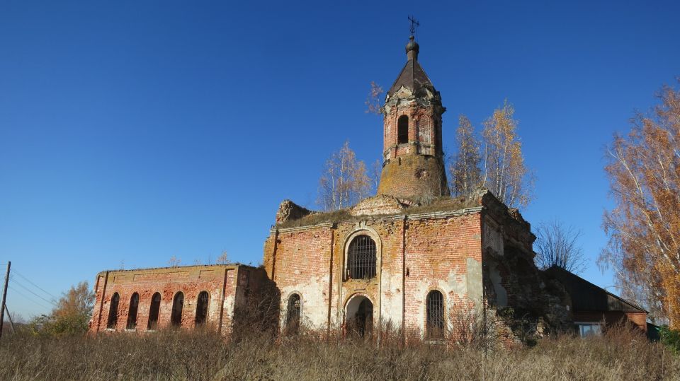 Ruined brick church with a bell tower against a clear blue sky.