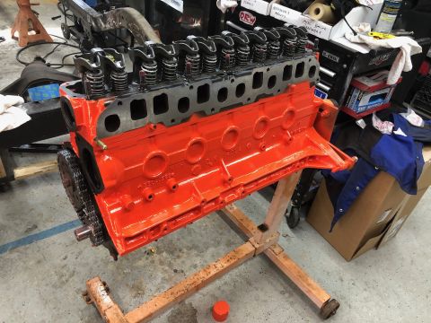 1992 Jeep Wrangler - A bright orange V8 engine block is mounted on an engine stand, with the cylinder head and rocker arms installed. The front timing chain and…