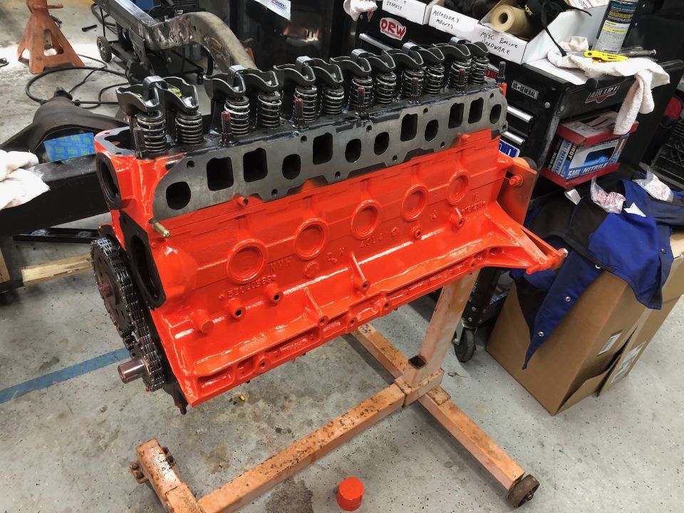 Orange V8 engine block on stand with cylinder head and timing chain visible