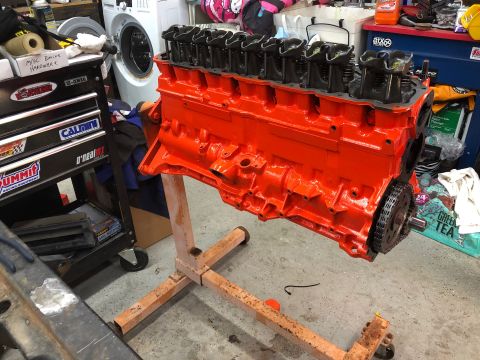 1992 Jeep Wrangler - An orange engine block with black valve covers is mounted on an orange engine stand in a garage. Various tools and automotive parts are vis…