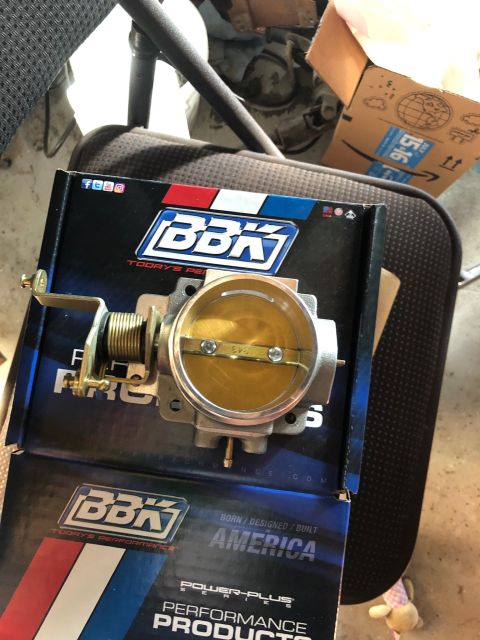 1992 Jeep Wrangler - A new BBK Performance throttle body is shown in its box, resting on a chair. The throttle body has a brass plate and a spring-loaded mechan…