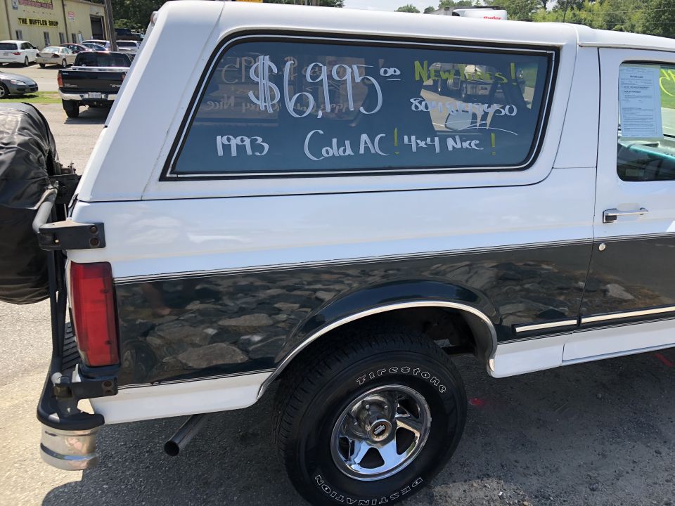 White and green 1993 Ford Bronco with $6,995 sale info written on rear window, parked on gravel