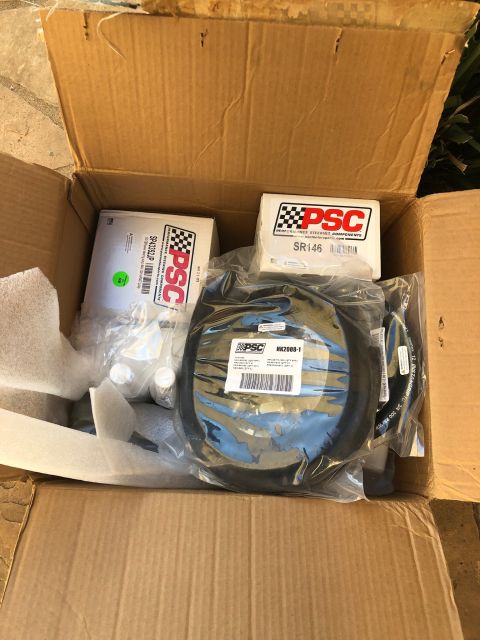 1992 Jeep Wrangler - An open cardboard box containing various PSC Performance Steering Components parts, including hoses and boxed components with labels.