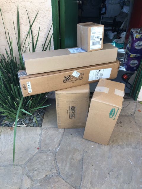 1992 Jeep Wrangler - Several cardboard boxes are stacked on a stone patio in front of a doorway. Some boxes have shipping labels and logos visible.