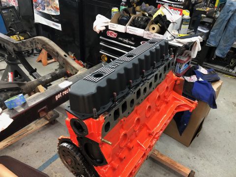 1992 Jeep Wrangler - A freshly painted orange engine block with a black valve cover is shown in a workshop setting. The engine is mounted on an engine stand, wi…