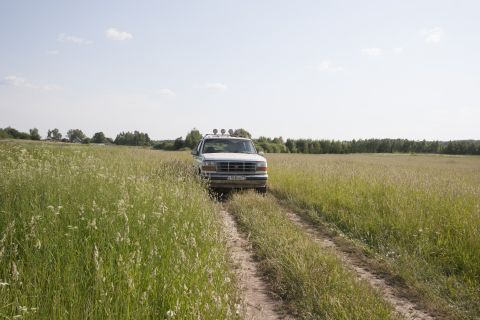 1993 Ford Bronco - A white Ford Bronco is parked on a dirt road in a field of tall grass. The vehicle has four auxiliary lights mounted on the roof rack.