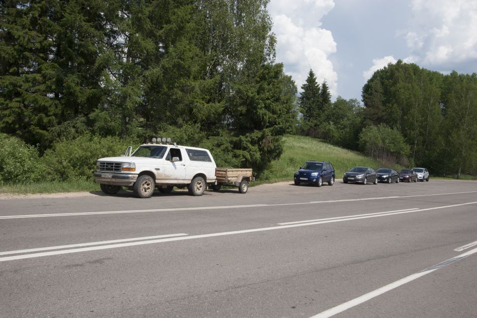 White 1993 Ford Bronco with trailer parked on roadside next to other cars.