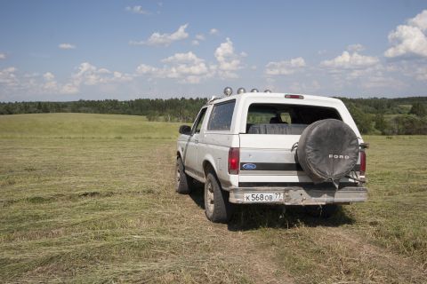 1993 Ford Bronco - A white Ford Bronco is parked in a grassy field with a wooded area in the background under a partly cloudy sky.