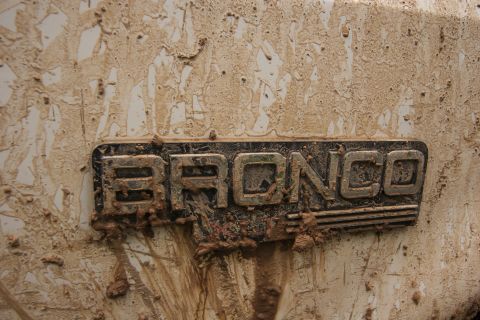 1993 Ford Bronco - A close-up of the "BRONCO" emblem on a dirty vehicle. The emblem is metallic and appears to be silver or chrome, with the letters filled wi…