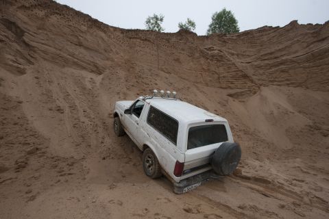 1993 Ford Bronco - A white 1993 Ford Bronco is parked on a sandy incline with a large sand dune behind it. The vehicle has a spare tire mounted on the rear an…