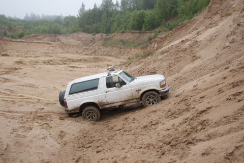 1993 Ford Bronco - A white Ford Bronco is driving up a steep sand dune in a quarry. The vehicle is covered in sand and appears to be stuck.