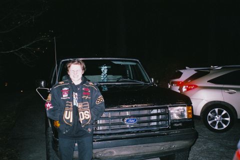 1988 Ford Bronco - A young person stands in front of a black Ford truck at night. A silver SUV is parked to the right of the truck.