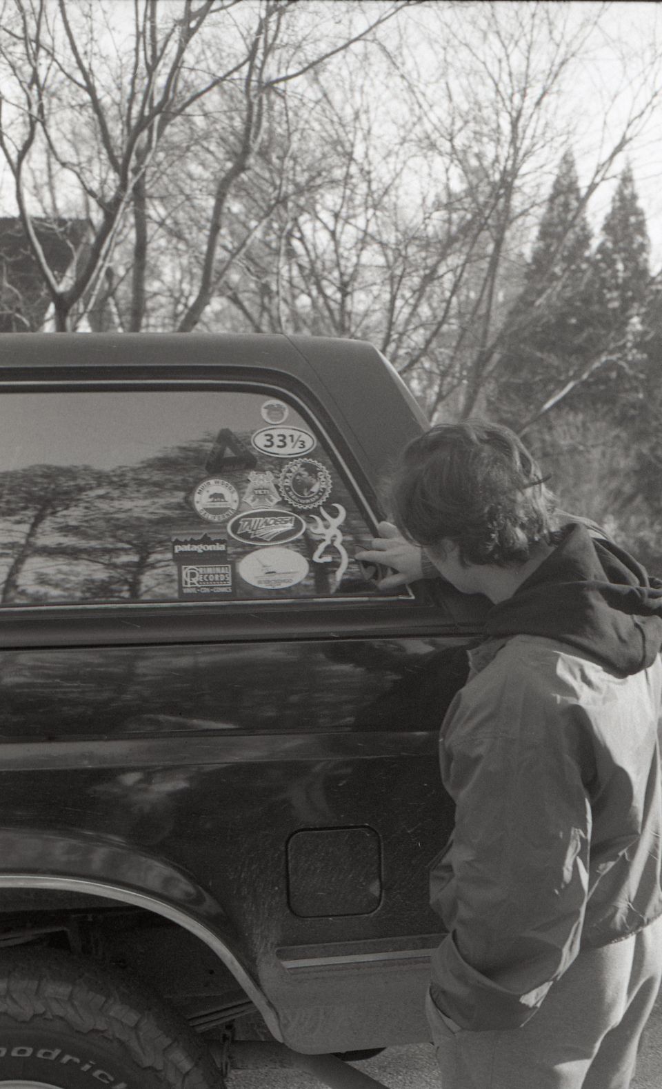 Person looking at stickers on the rear window of a dark SUV with a camper shell.