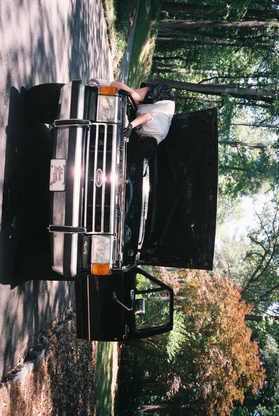 Person working on the engine of a black 1988 Ford Bronco.