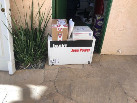 1992 Jeep Wrangler - Several delivery boxes are stacked on top of each other in front of a doorway. The largest box has "Banks" and "Jeep Power" printed on it.