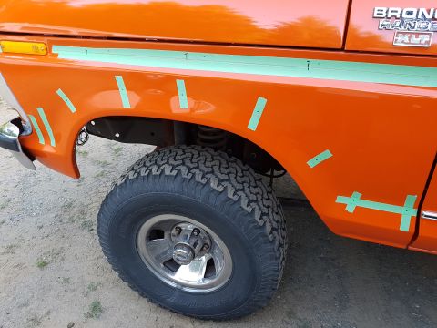 1978 Ford Bronco - The right front fender of an orange 1978 Ford Bronco is shown with green masking tape applied in a grid pattern. A portion of the front tir…