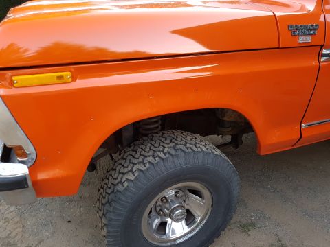 1978 Ford Bronco - Close-up of the front passenger side fender and wheel of an orange 1978 Ford Bronco. The vehicle has a chrome bumper and a yellow side mark…