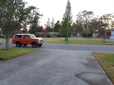 1978 Ford Bronco - A bright orange 1978 Ford Bronco with a white top is parked on a concrete driveway next to a street. The classic SUV is viewed from the sid…