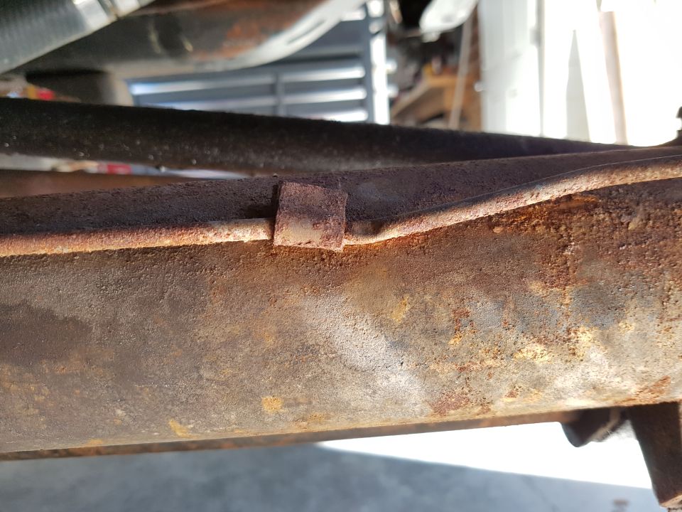 Close-up of a rusted metal frame with visible bolts and a copper pipe