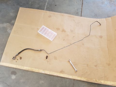 1978 Ford Bronco - Photograph of an actual hydraulic hose assembly, fittings, and a turnbuckle on cardboard, not a document.