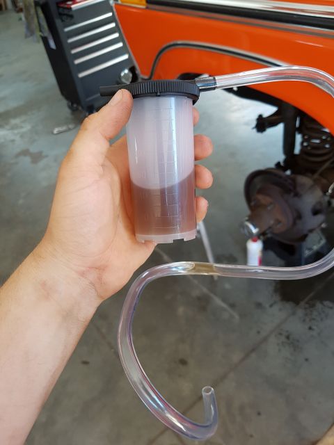 1978 Ford Bronco - Using a brake fluid bleeder tool during maintenance on an orange vehicle.