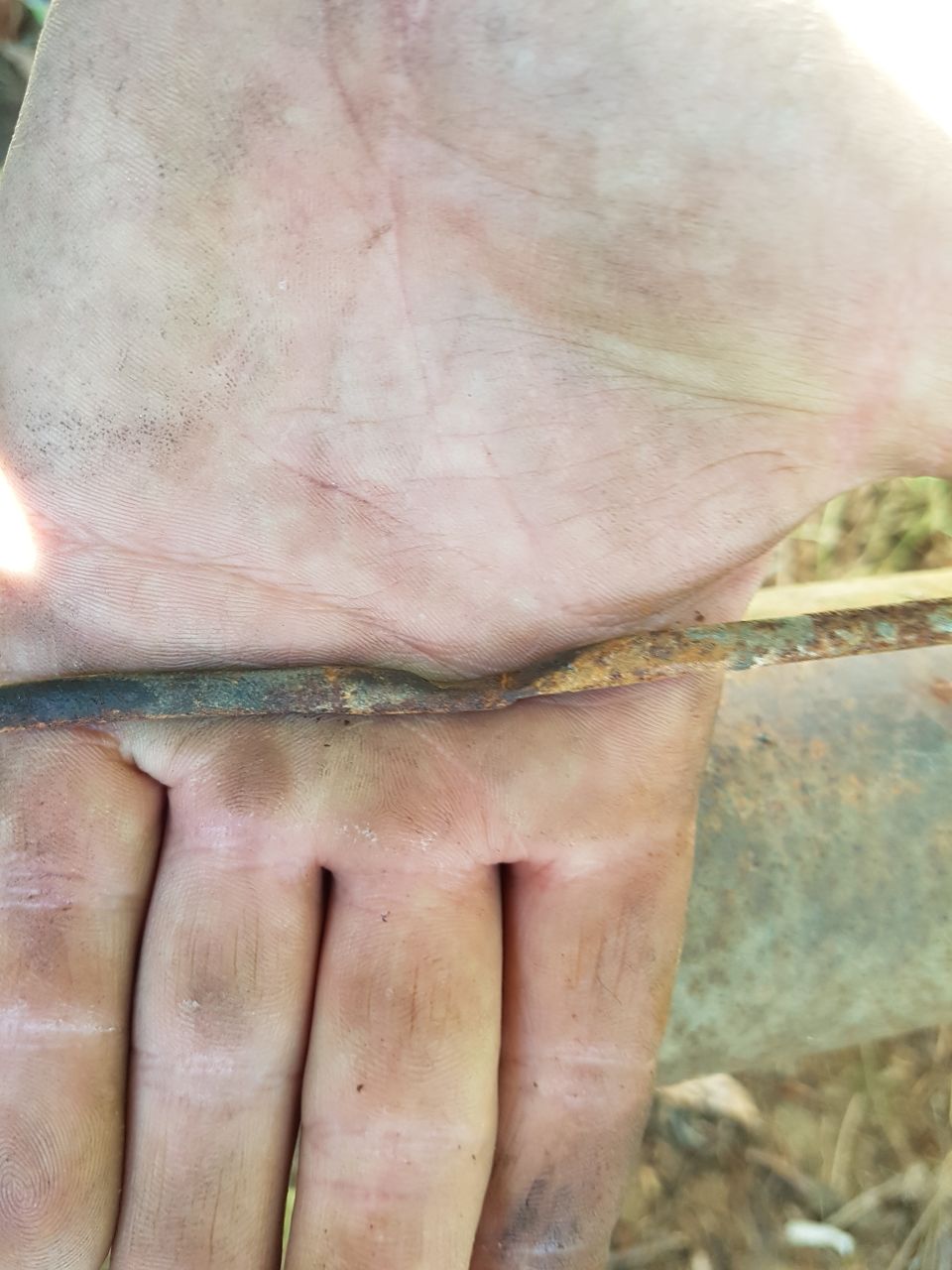 rusty metal rod resting on a dirty hand