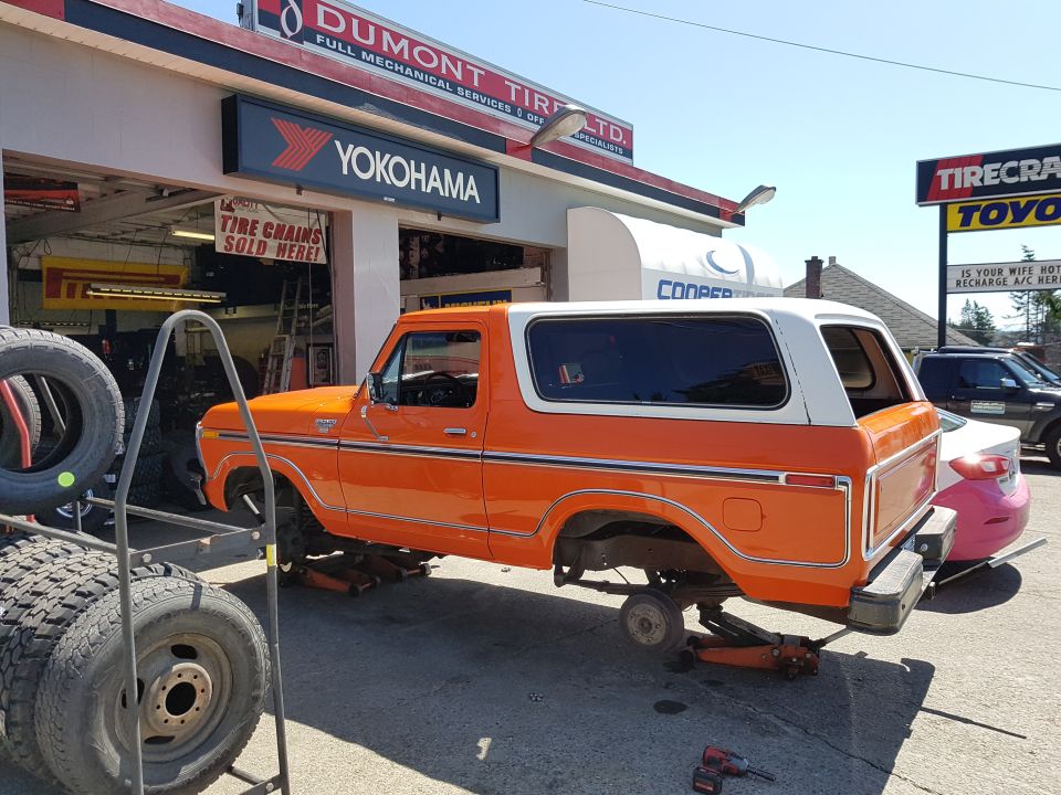 Orange and white 1978 Ford Bronco on jacks, missing front wheels, at a tire shop