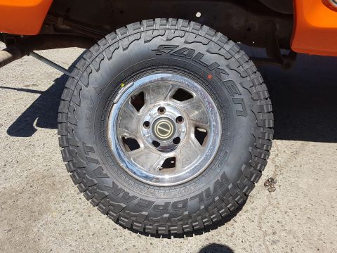 1978 Ford Bronco - Falken Wildpeak A/T tire mounted on a chrome wheel, part of an orange vehicle.