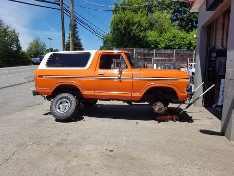 1978 Ford Bronco - This orange 1978 Ford Bronco is being serviced at a garage, with one wheel removed.