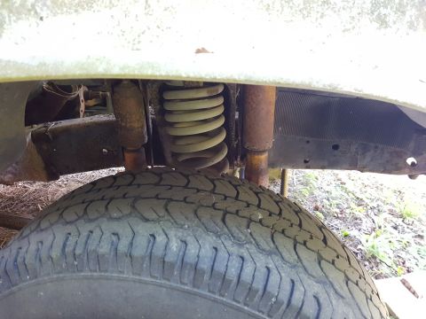1978 Ford Bronco - Front tire and suspension detail of a vehicle, showing rust on the shock absorber and spring.